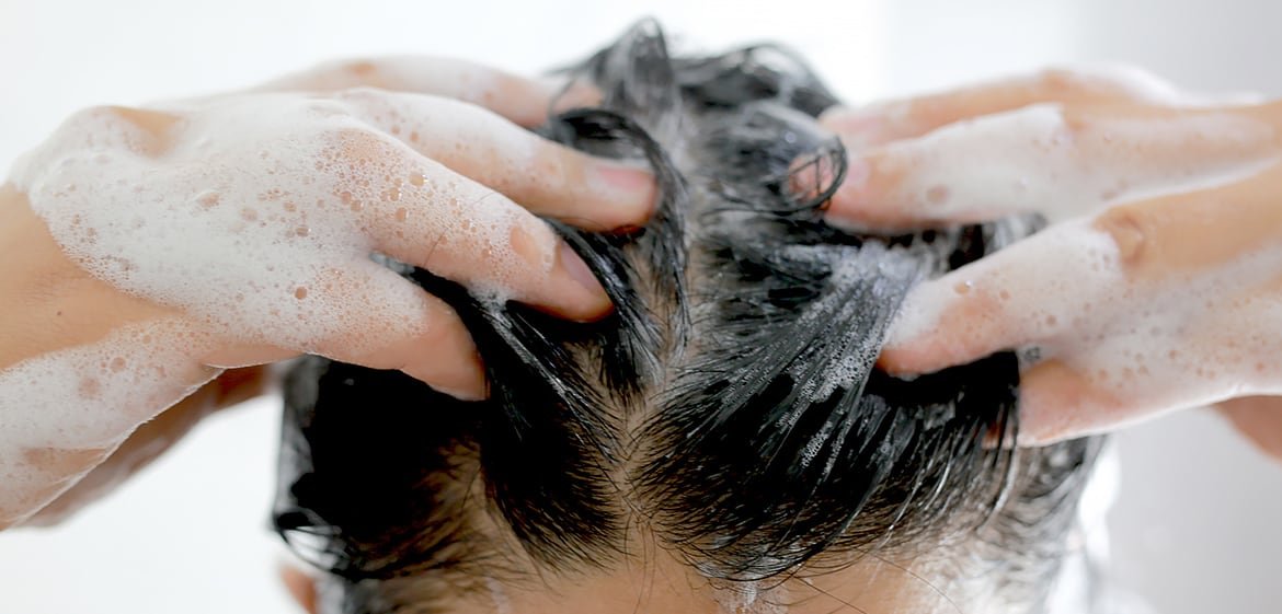 Frau shampooniert ihre braunen Haare ein.